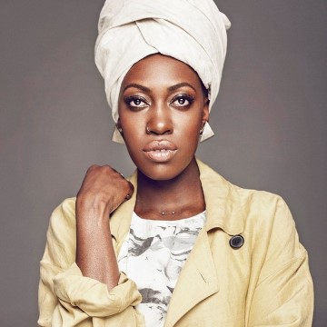 The image features a person wearing a white headdress and a white turban. The individual in the photo is Tonye Aganaba, a singer.