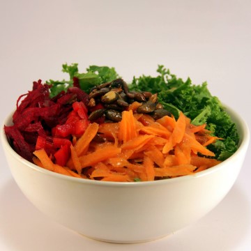The image is a bowl of vegetables, specifically a Buddha bowl, containing ingredients such as leafy greens, carrots, and other salad components. It is a vegetarian food option.