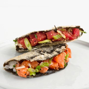 The image shows a taco with salmon and tuna, made of nori. The taco appears to be a snack or fast food item, with green onion as one of the garnishes.