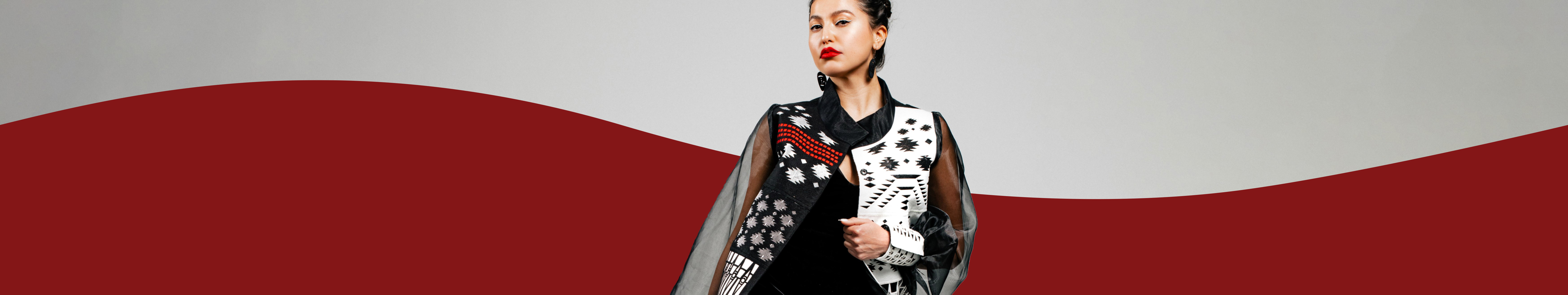 The image features a model wearing a black and white dress against a white background. The person is likely part of a fashion show celebrating Indigenous fashion by Himikalas Pamela Baker.