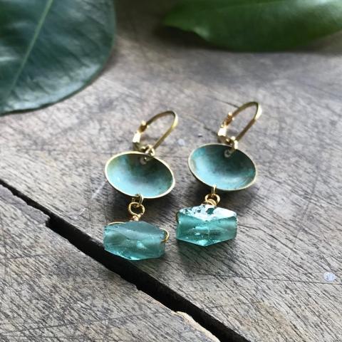The image is a set of Effie Baker Designs earrings placed on a table. The earrings feature turquoise gemstones and green enamel, with copper elements.