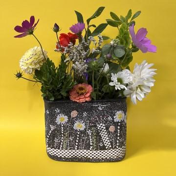 The image is a basket of flowers. It features a variety of flowers in different colors. The arrangement is likely a product of the Red Pot Pottery Company and may include elements like cut flowers, petals, and a mix of indoor plants.