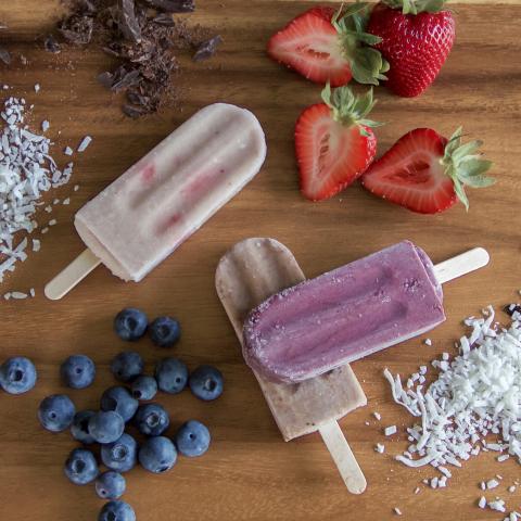 The image shows a group of different foods, including fruit such as strawberries and popsicles, along with coconut flakes and chocolate The setting appears to be indoors on a table. Additionally, there is a mention of RICO 'N LALO popsicles in the additional context.