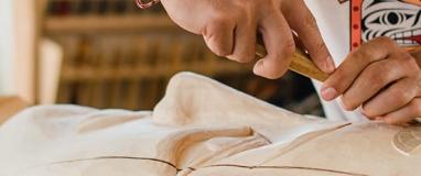 The image shows a person's hands on a white cloth, and the additional context mentions a carver working with wood.